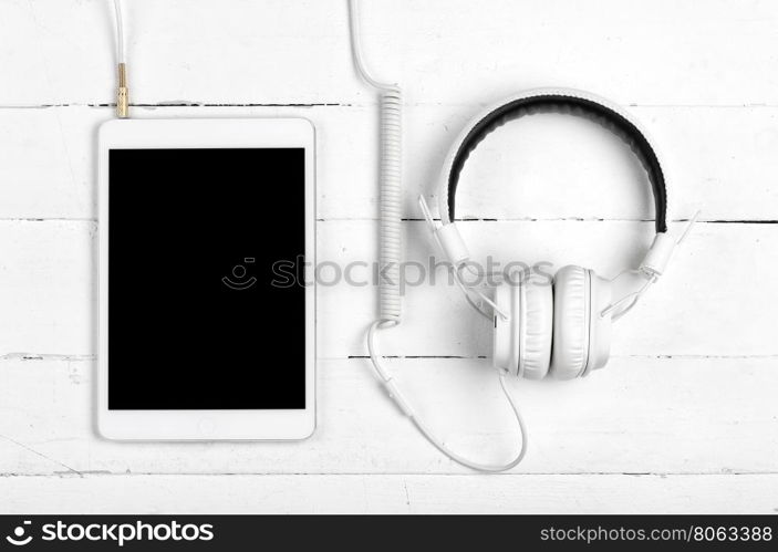 White tablet with headphones on white wooden background. White tablet with headphones