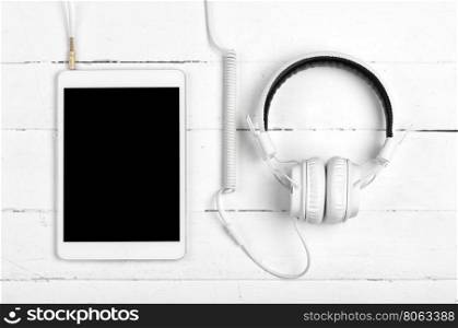 White tablet with headphones on white wooden background. White tablet with headphones