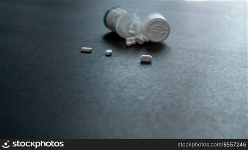 White tablets pills and blur plastic pill bottle on dark floor. Prescription drugs. Pharmaceutical industry. Medical care. Medication for cure illness. Pharmacy. Small white pills. Dose recommended.
