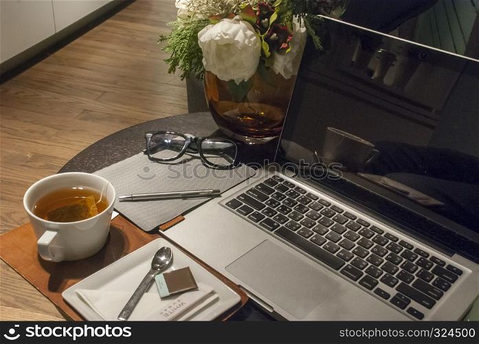 White tea cup on a wooden desk With a rose vase placed Open the laptop and work in the living room at home.