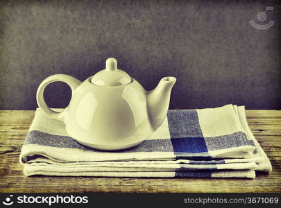 White teapot and dishcloth on old wooden table over green background