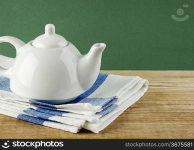 White teapot and dishcloth on old wooden table over green background