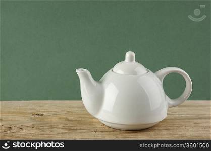 White teapot on old wooden table over green background