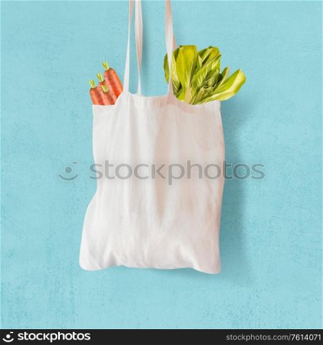 White textile grocery shopping bag with vegetables hanging at light blue background. Copy space. Zero waste concept. Cotton reusable bag. Plastic free shopping. Eco friendly bag mock up.