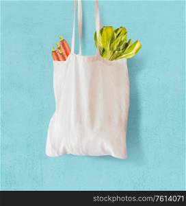 White textile grocery shopping bag with vegetables hanging at light blue background. Copy space. Zero waste concept. Cotton reusable bag. Plastic free shopping. Eco friendly bag mock up.