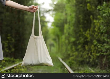white tote bag canvas fabric with handle mock up design. Close up of woman’s hand holding eco or reusable shopping bag on green outdoor background. No plastic bag and ecology concept. white tote bag canvas fabric with handle mock up design. Close up of woman’s hand holding eco or reusable shopping bag on green outdoor background. No plastic bag and ecology concept.