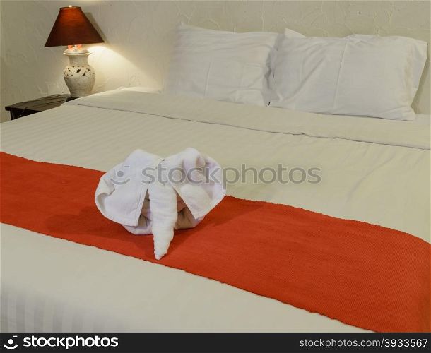 White towel in elephant shape on white bed in Thai style hotel bedroom