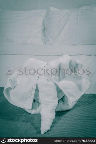 White towel in elephant shape on white bed in Thai style hotel bedroom. Vintage style color.
