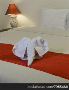 White towel in elephant shape on white bed in Thai style hotel bedroom