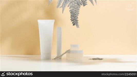 white tube for cosmetics, a jar of cream and silver leaf on a white table. Cosmetic on a beige shadow background. Cream bottle, lotion, cleanser, shampoo for skincare