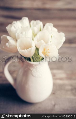 White tulips in a vase in pastel colors on rustic background