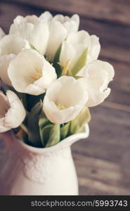 White tulips in a vase in pastel colors on rustic background