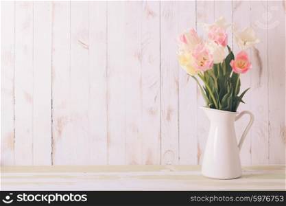 White vase with delicate shades armful of tulips on a wooden background. Flowers bouquet of white and pink tulips