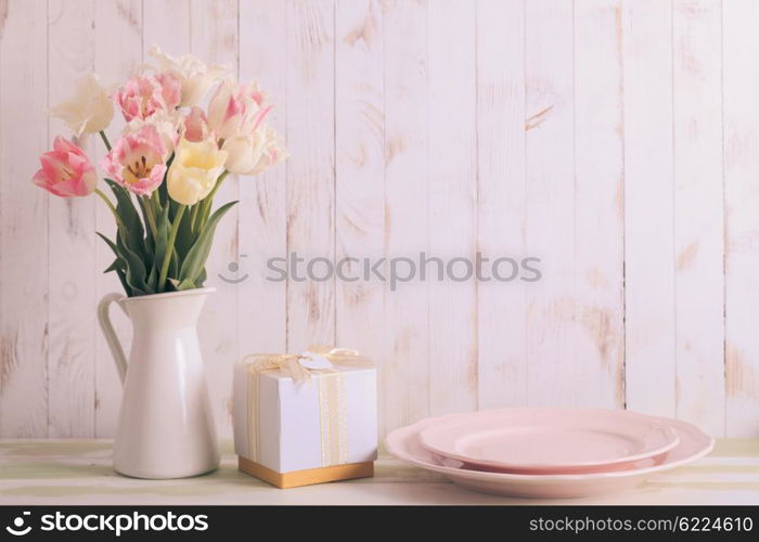 White vase with delicate shades armful of tulips on a wooden background. Flowers bouquet of white and pink tulips