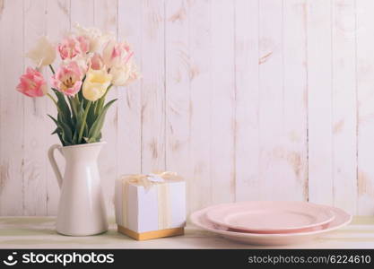 White vase with delicate shades armful of tulips on a wooden background. Flowers bouquet of white and pink tulips