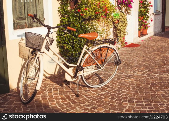White vintage bicycle with basket on vintage house wall in Italy. Retro bycicle in Italy