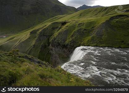 White water flowing over a cliff surrounded by green meadows in the mountains