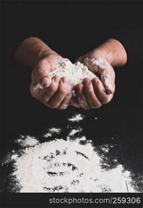 white wheat flour in male hands, black background, vintage toning