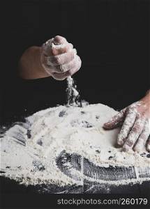 white wheat flour on a black wooden table and the cook prepare to knead the dough