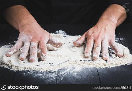white wheat flour on a black wooden table and two male hands, close up
