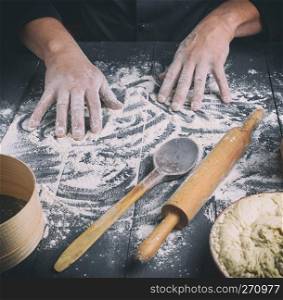 white wheat flour on a black wooden table and two male hands, close up