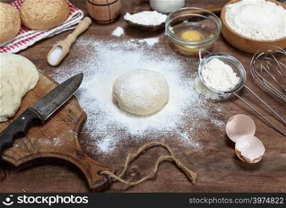 white wheat flour round dough and ingredients on a brown wooden table