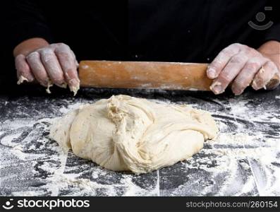 white wheat flour round dough and wooden rolling pin in male hands