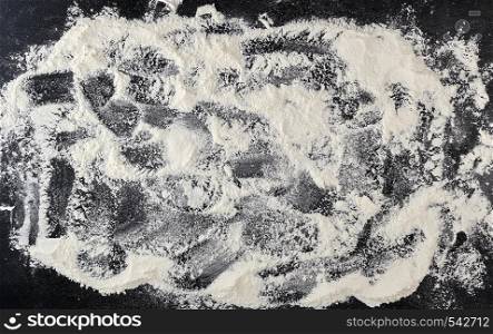 white wheat flour scattered on a black background, product is spread over the surface, kitchen background, top view