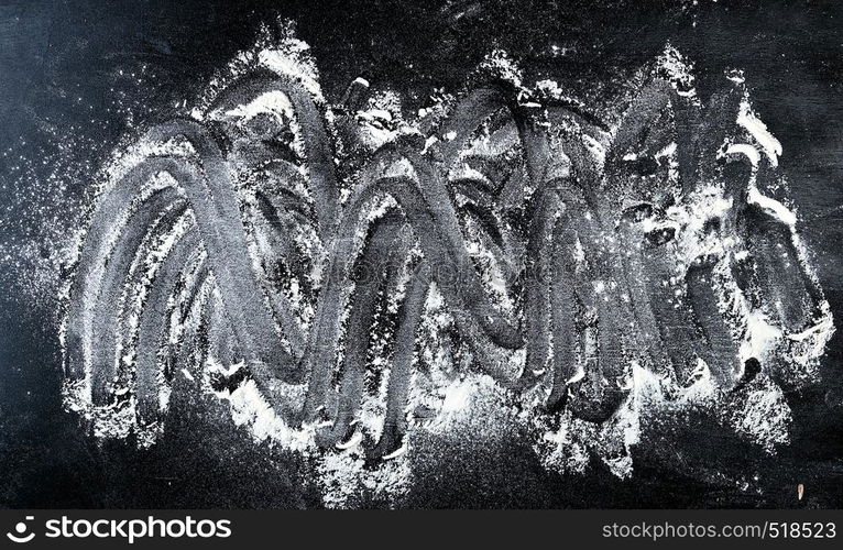 white wheat flour scattered on a black background, the product is spread over the surface, kitchen background, top view