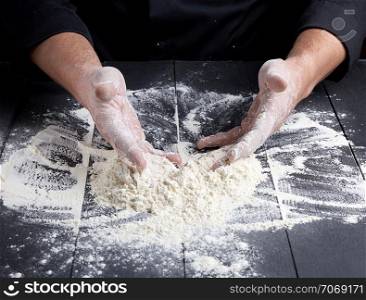 white wheat flour scattered on a wooden wooden table, the chef in uniform uniforms hands the product