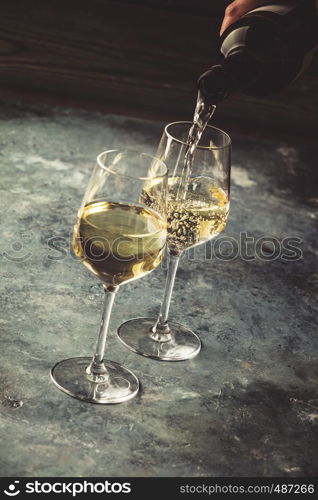 White wine pouring into glasses on the stone background