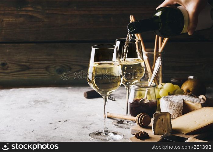 White wine pouring into glasses with charcuterie assortment on the stone background