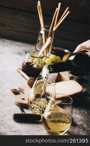 White wine pouring into glasses with charcuterie assortment on the stone background