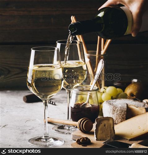 White wine pouring into glasses with charcuterie assortment on the stone background. White wine pouring into glasses with charcuterie assortment
