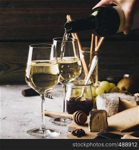 White wine pouring into glasses with charcuterie assortment on the stone background. White wine pouring into glasses with charcuterie assortment