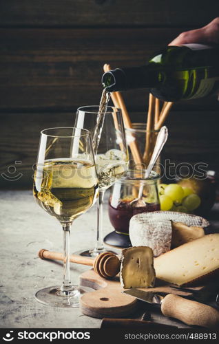 White wine pouring into glasses with charcuterie assortment on the stone background. White wine pouring into glasses with charcuterie assortment