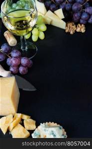 White wine, various types of cheese, walnuts and grapes on a black slate stone background