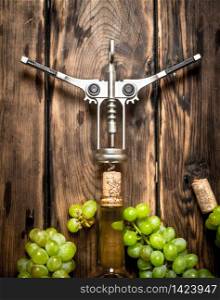 White wine with a corkscrew and branches of grapes. On a wooden table.. White wine with a corkscrew and branches of grapes.