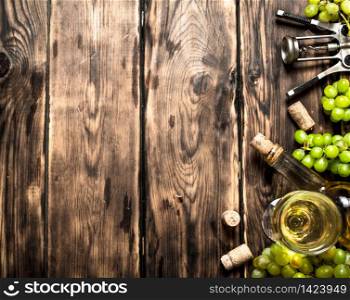 White wine with a corkscrew and branches of grapes. On a wooden table.. White wine with a corkscrew and branches of grapes.