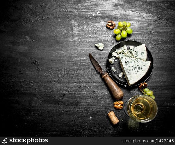 white wine with a slice of cheese with blue mold. On a black wooden background.. white wine with slice of cheese