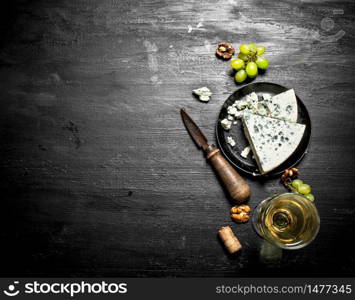 white wine with a slice of cheese with blue mold. On a black wooden background.. white wine with slice of cheese