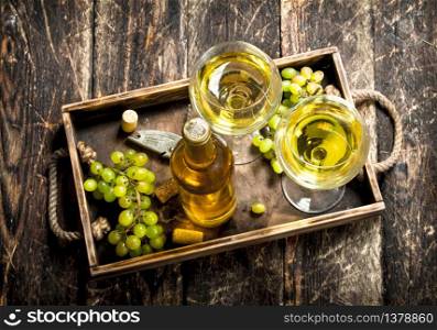 White wine with fresh grapes on an old tray. On a wooden background.. White wine with fresh grapes on an old tray.
