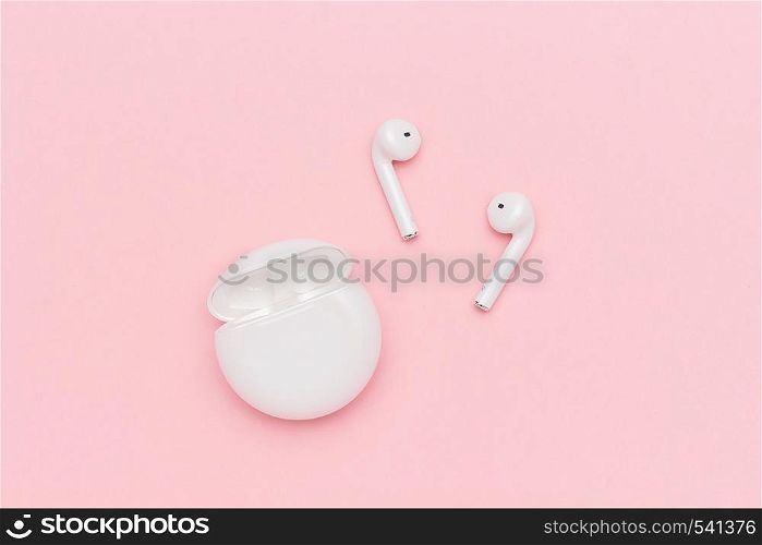 White wireless Bluetooth headphones and charging case on pink paper background.. Novosibirsk, Russia - March 22, 2019: White wireless Bluetooth headphones and charging case on pink paper background