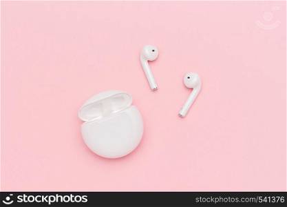 White wireless Bluetooth headphones and charging case on pink paper background.. Novosibirsk, Russia - March 22, 2019: White wireless Bluetooth headphones and charging case on pink paper background
