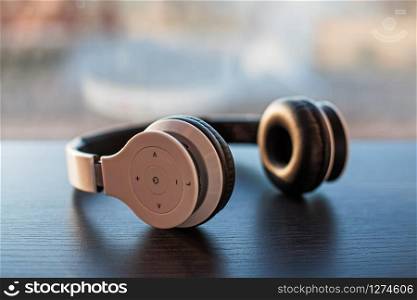 White wireless headphones placed on laminated dark wooden surface on a blurred window glass background colored by sunlight.