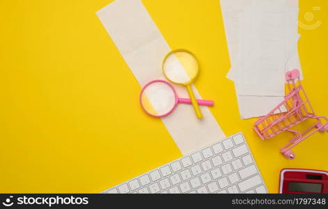 white wireless keyboard, stack of paper receipts and magnifier on yellow background, budget analysis concept, savings