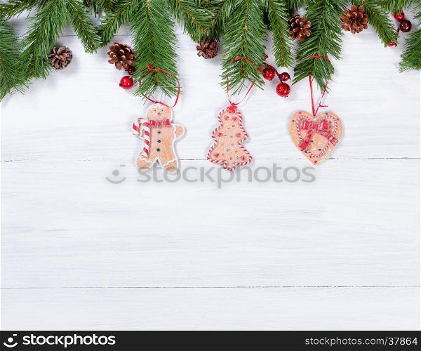 White wooden background with cookies hanging from fir branches for Christmas concept.