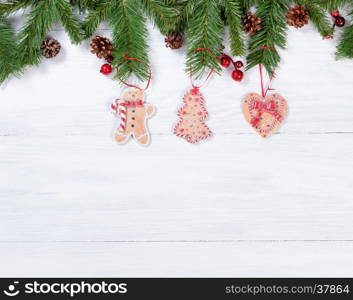 White wooden background with cookies hanging from fir branches for Christmas concept.