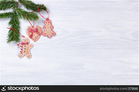 White wooden background with cookies hanging from fir branches on upper left corner.