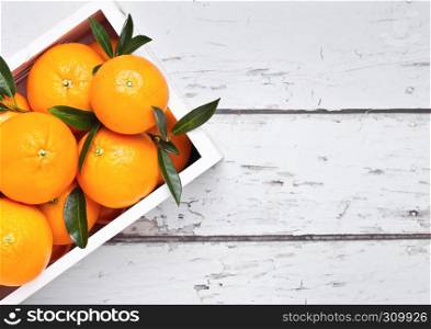 White wooden box with fresh raw organic oranges on light wooden background.Top view.